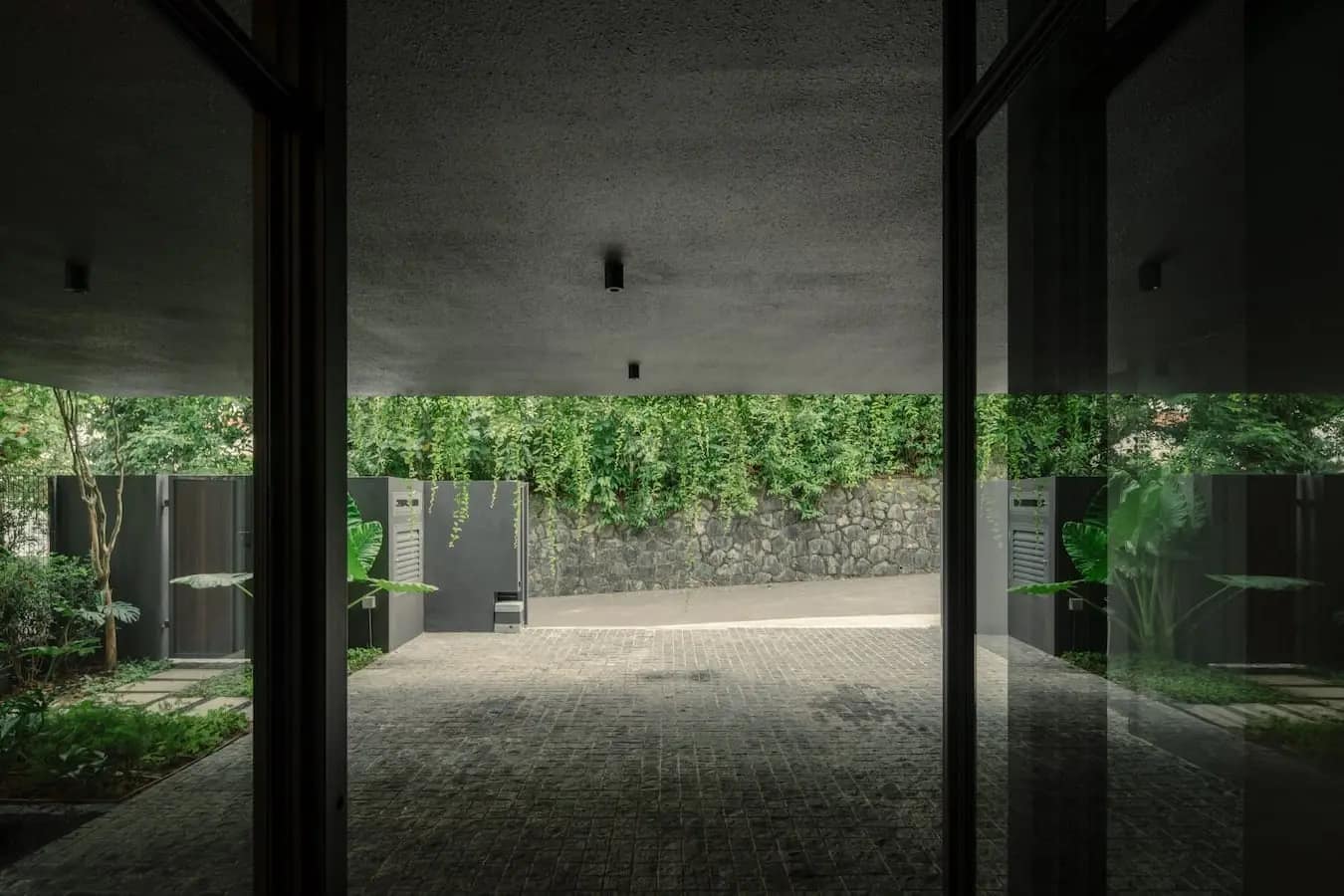 Covered arrival court looking out to a stone boundary wall and dense planting