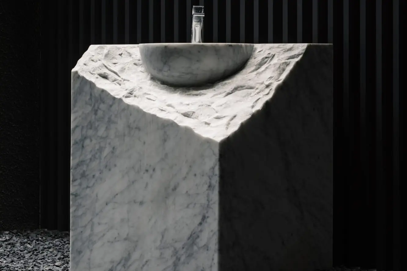 Basin carved from a single block of Carrara marble against a black fluted wall