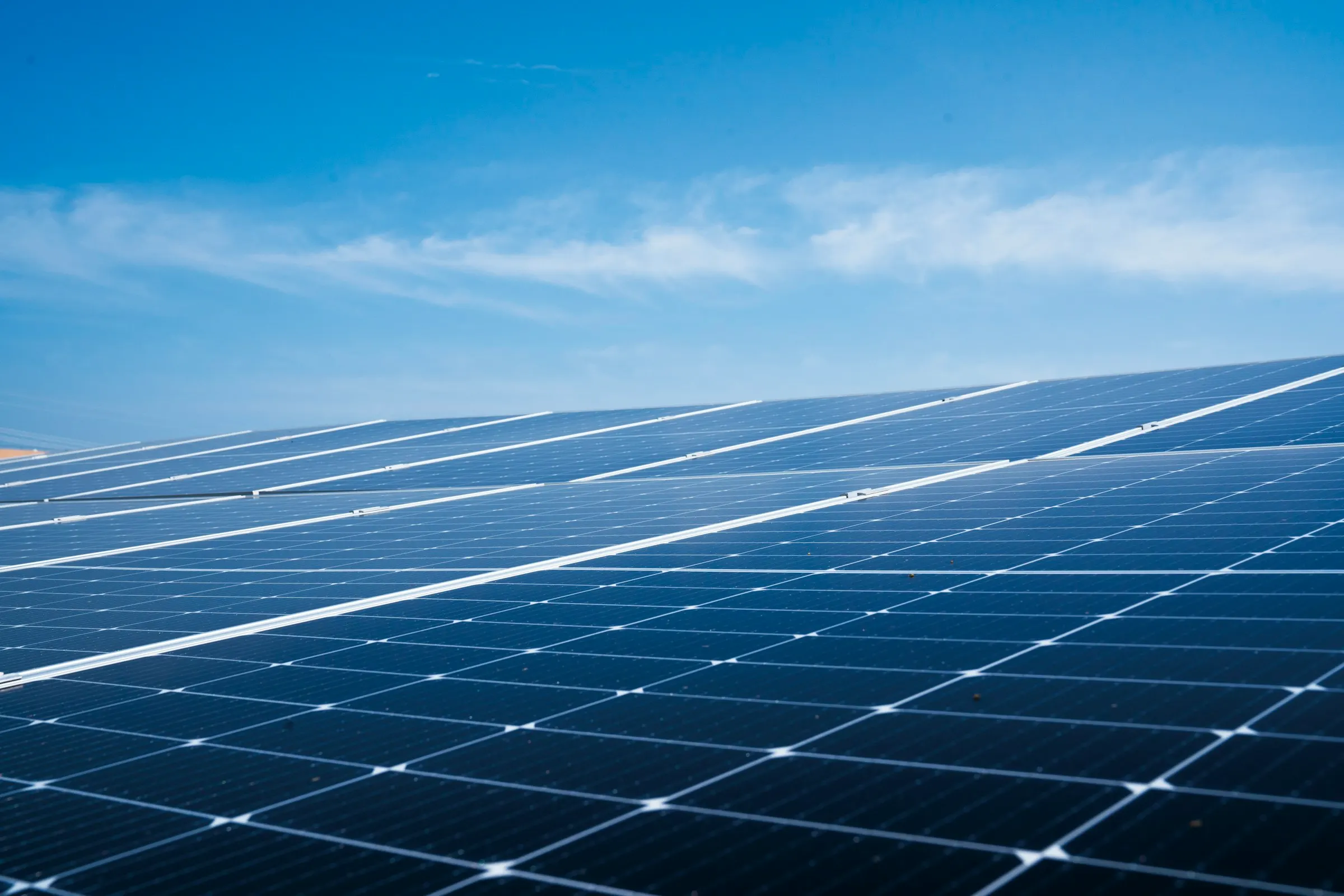 Rows of solar panels on a roof under a clear blue sky.